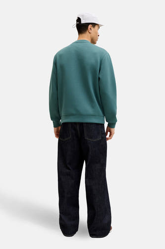 Blauwe sweater van CORE BY JACK & JONES, gezien van achteren, gecombineerd met wijde jeans en een witte pet.
