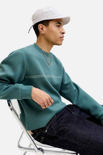 Blauw sweatshirt van CORE BY JACK & JONES met lange mouwen en een ronde hals, gecombineerd met een zilveren ketting en een witte pet.
