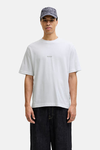 T-shirt blanc à manches courtes de CORE BY JACK & JONES, porté avec des jeans larges foncés et un chapeau à motif.