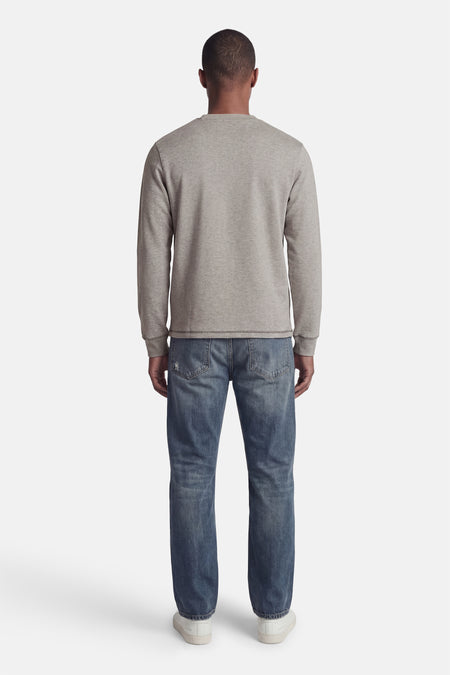 Pull gris de CORE BY JACK & JONES, à manches longues, col rond et poignets côtelés, porté de dos sur un jean bleu et des baskets blanches.