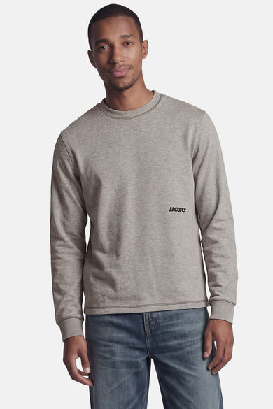 Sweatshirt chiné gris de CORE BY JACK & JONES avec col rond, logo 'JJCare' sur la poitrine et coutures apparentes, porté par un homme sur un jean.