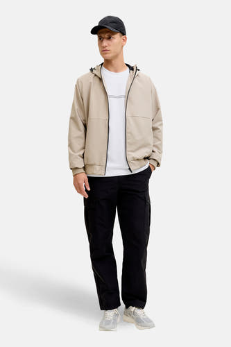 Wit T-shirt met korte mouwen van CORE BY JACK & JONES, gedragen onder een beige jas met zwarte cargobroek en grijze sneakers.