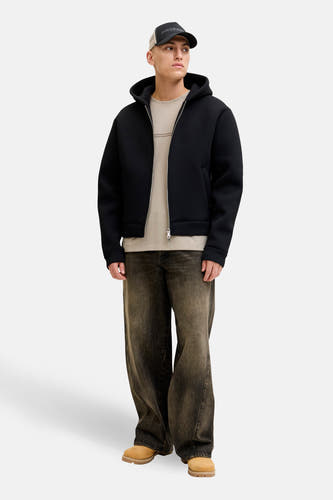 Beige T-shirt met korte mouwen van CORE BY JACK & JONES, gedragen met een zwarte jas met capuchon, bruine jeans en schoenen.