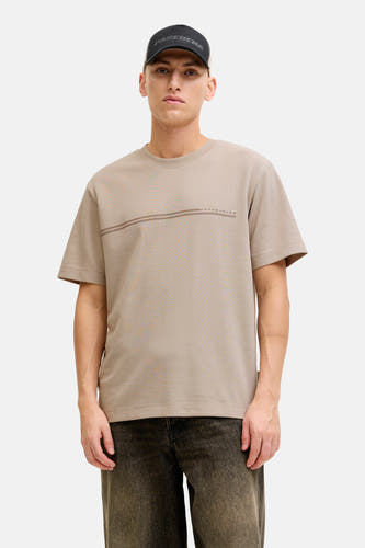 Beige T-shirt met korte mouwen van CORE by JACK & JONES, met twee horizontale strepen en zwarte jeans.

