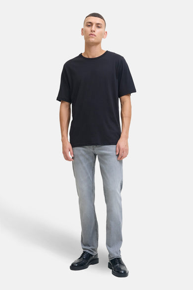 Lichtgrijze slim fit jeans van JACK & JONES JEANS INTELLIGENCE, gecombineerd met een zwart T-shirt en zwarte nette schoenen.
