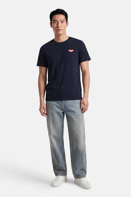 Blauw T-shirt met korte mouwen van CORE BY JACK & JONES, met rode logo op de borst, gecombineerd met jeans en witte sneakers.