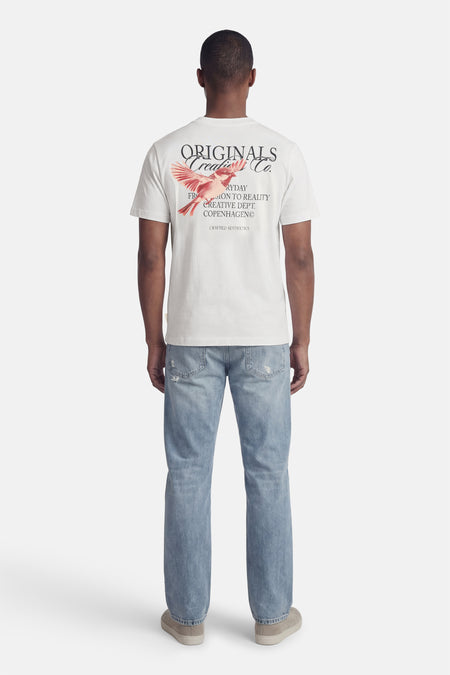 Wit T-shirt met korte mouwen van ORIGINALS BY JACK & JONES, met print van een vogel op de achterkant, gecombineerd met blauwe jeans en suède schoenen.