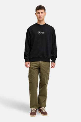 Zwarte sweater van JJREBEL met een logo op de borst, gecombineerd met kaki broeken en bruine schoenen.
