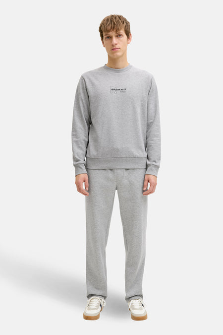 Grijze sweater met ronde hals van JJREBEL, met een kleine print op de borst, gedragen met een bijpassende joggingbroek en witte sneakers.
