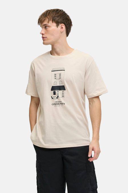 Beige T-shirt met korte mouwen van JJREBEL, met een gebouwopdruk en gedragen met zwarte broek.
