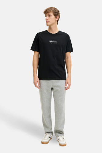T-shirt noir à manches courtes de JJREBEL, avec un petit imprimé sur la poitrine, combiné avec un jogging gris et des baskets blanches.