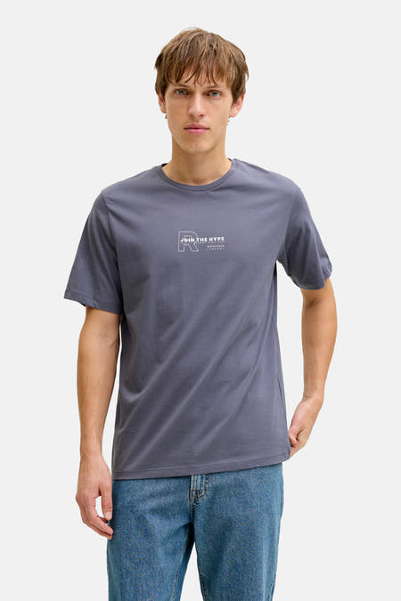 Blauw T-shirt met korte mouwen van JJREBEL, gedragen met een jeansbroek en effen achtergrond.
