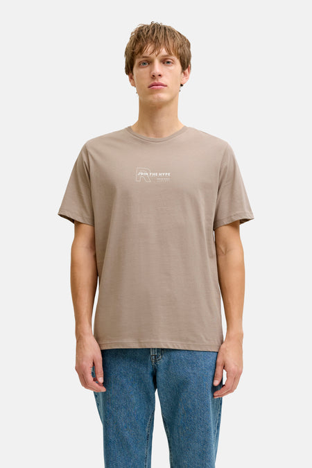 Bruin T-shirt met korte mouwen van JJREBEL, met witte print op de borst, gecombineerd met blauwe jeans.
