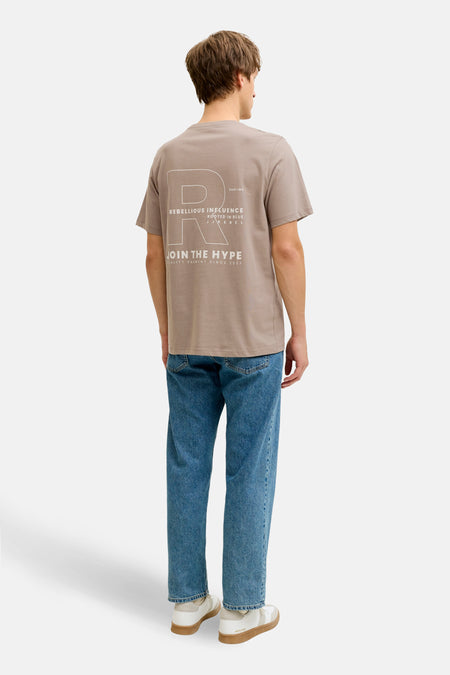 T-shirt marron à manches courtes de JJREBEL, avec imprimé blanc au dos, combiné avec un jean bleu et des baskets blanches.