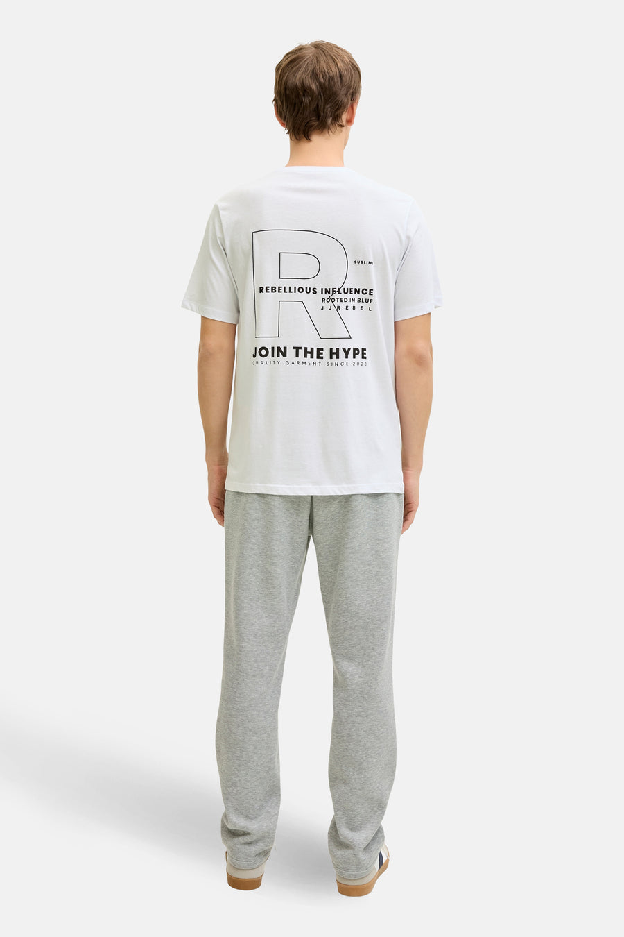 T-shirt blanc à manches courtes de JJREBEL, avec un imprimé graphique au dos, porté avec un jogging gris et des baskets.