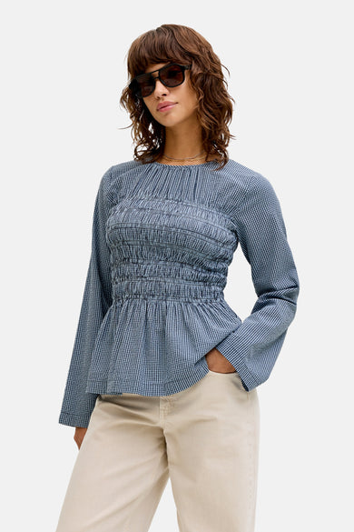 Blouse bleue à manches longues de JJXX, avec un détail smocké et portée avec un pantalon crème et des sandales.
