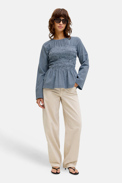 Blauw, lange mouwen blouse van JJXX, met een smock-detail en gedragen met crèmekleurige broek en sandalen.
