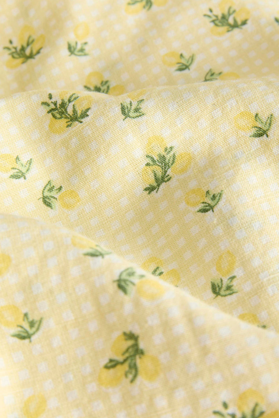 Geel kleedje van JJXX met ruitjespatroon en citroenprint, close-up van gevouwen stof.