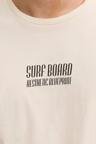 T-shirt écru de JJREBEL avec texte noir "Surf Board Aesthetic Blueprint", gros plan du haut du corps.