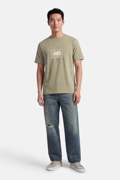 T-shirt vert à manches courtes ORIGINALS BY JACK & JONES, avec un imprimé rectangulaire, combiné avec un jean bleu et des baskets grises.