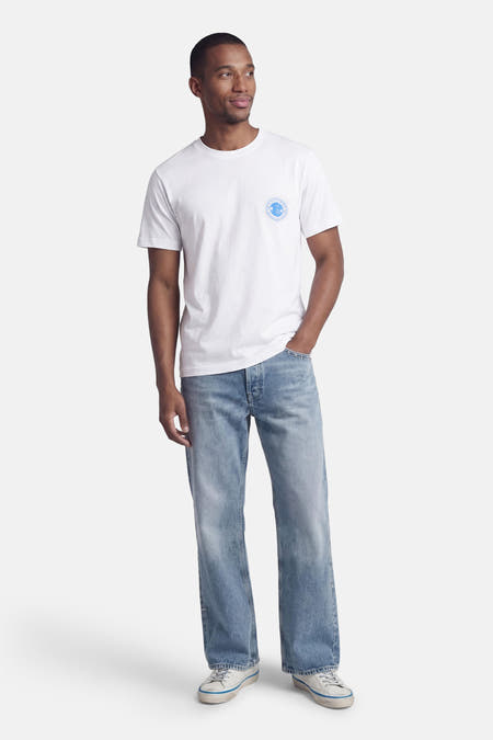 T-shirt blanc à manches courtes de ORIGINALS BY JACK & JONES, avec col rond et imprimé logo sur la poitrine, porté avec un jean et des baskets.