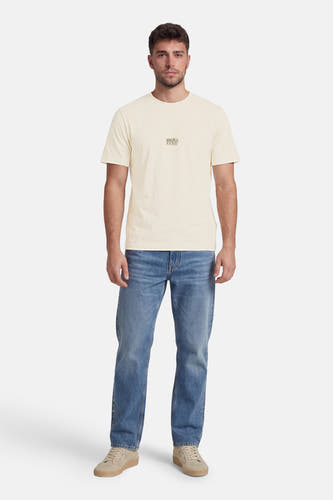 Ecru T-shirt van CORE BY JACK & JONES met klein logo op de borst, gedragen door een man met blauwe jeans en beige sneakers.