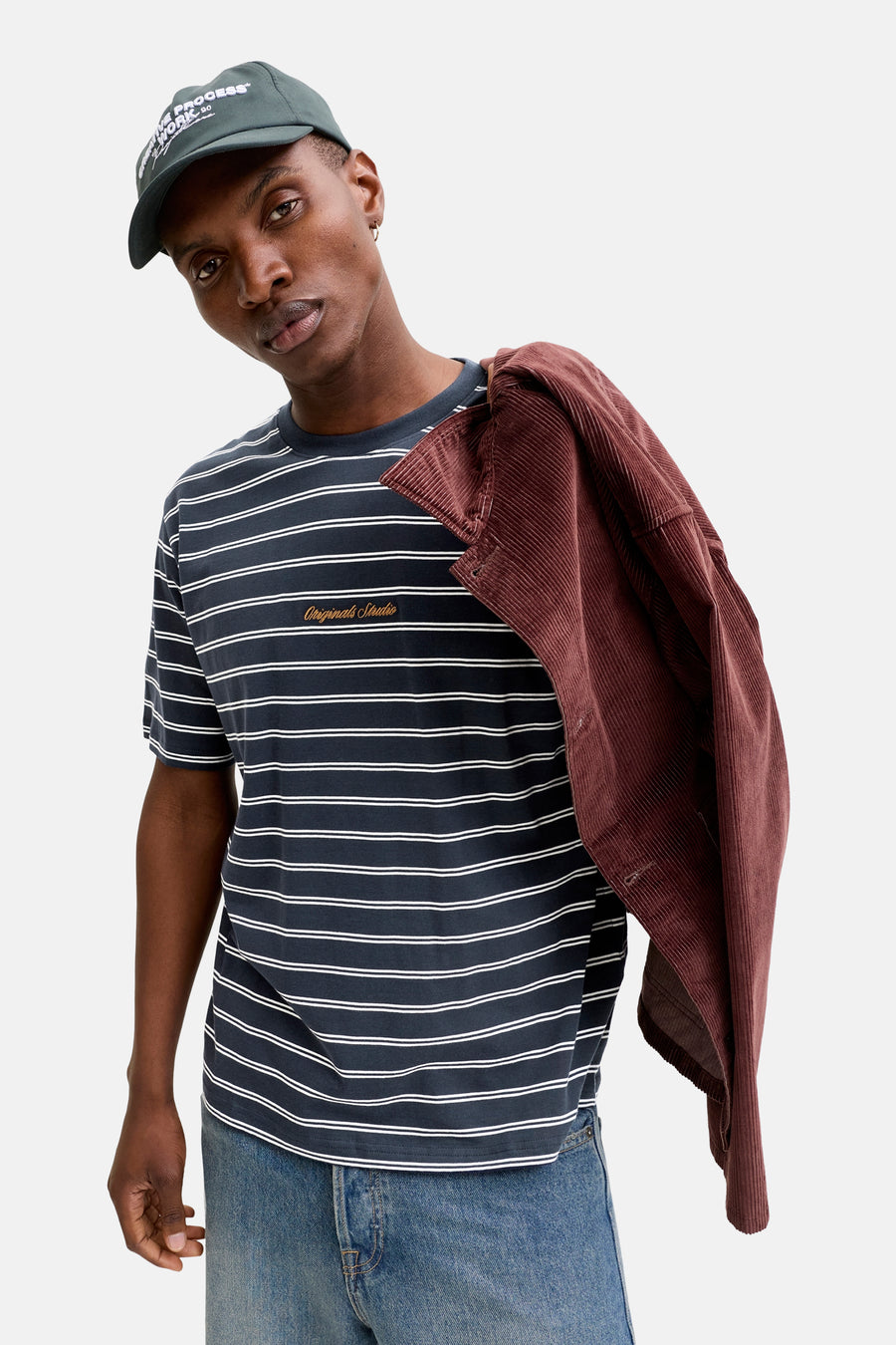 Blauw gestreept T-shirt van Originals by Jack & Jones, met een bordeauxrood jack over de schouder en een pet.