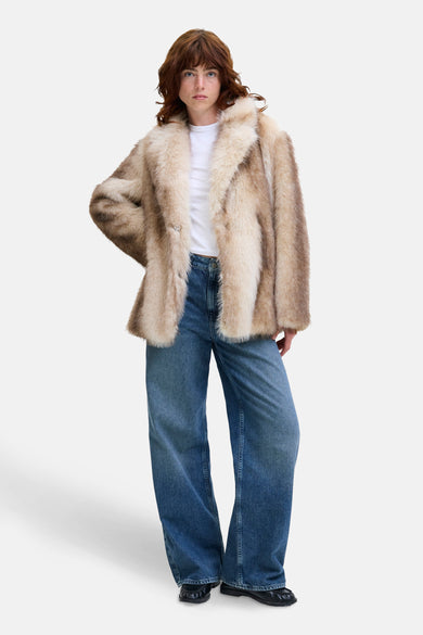 Korte ecru jas van JJXX, gedragen over een wit shirt en wijde jeans.