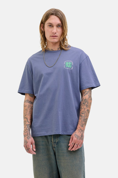 T-shirt bleu à manches courtes d'ORIGINALS BY JACK & JONES, avec une impression graphique sur la poitrine et porté avec une chaîne argentée.