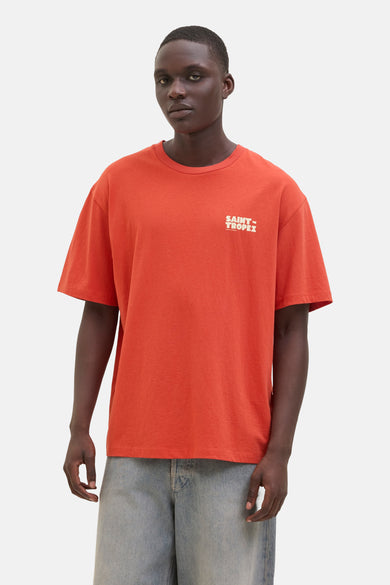 T-shirt orange à manches courtes d'ORIGINALS BY JACK & JONES, avec du texte "Saint Tropez" blanc, associé à un jean.