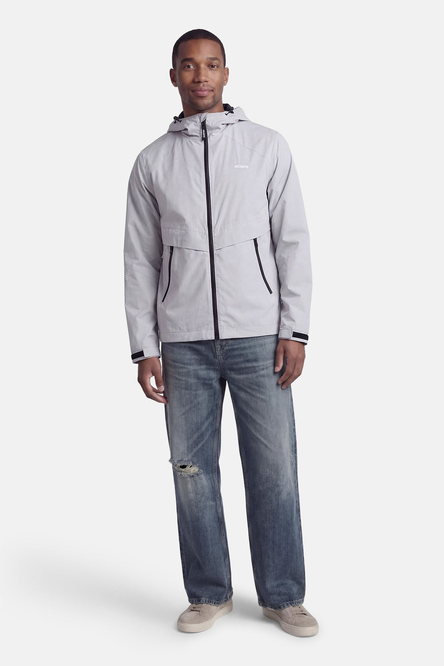 Veste courte grise de CORE BY JACK & JONES, avec capuche, poches zippées et portée avec un jean bleu et des baskets grises.
