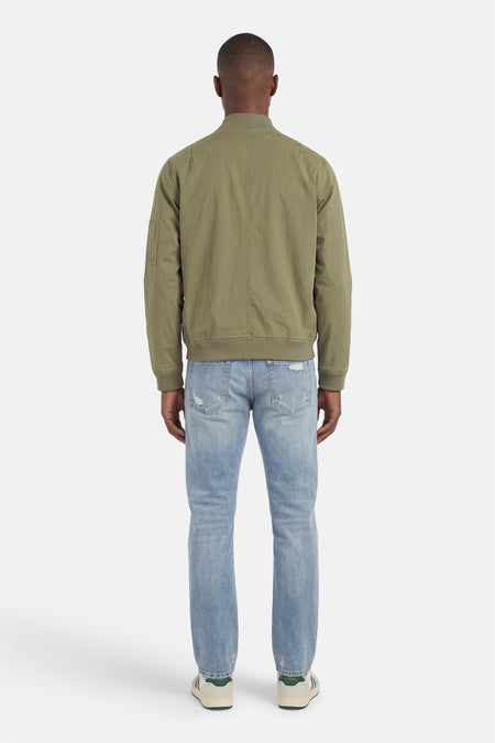 Veste courte verte de CORE BY JACK & JONES, vue de dos, avec texture tissée, poignets côtelés et poche sur la manche, portée avec un jean bleu clair et des baskets.