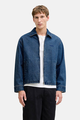 Jeansjas van mid blue denim van PREMIUM BLUE by JACK & JONES, met rits en witte blouse eronder, zwarte broek.

