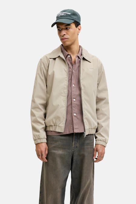 Manteau court beige de ORIGINALS BY JACK & JONES, avec une chemise à carreaux et un jean foncé.