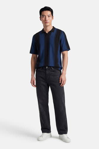 Multikleurige polo met korte mouwen van CORE BY JACK & JONES, met zwarte en blauwe strepen, gecombineerd met zwarte jeans en witte sneakers.

