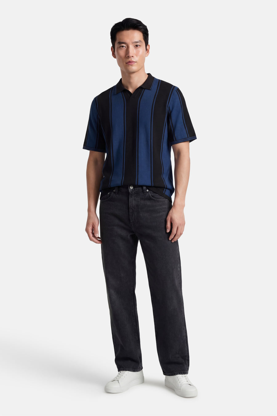 Multikleurige polo met korte mouwen van CORE BY JACK & JONES, met zwarte en blauwe strepen, gecombineerd met zwarte jeans en witte sneakers.
