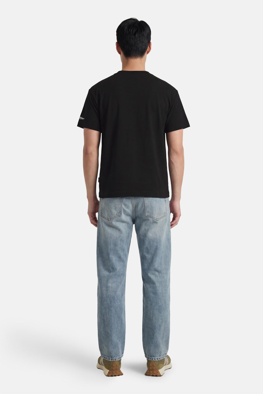 T-shirt noir à manches courtes de ORIGINALS BY JACK & JONES, sur un homme avec un jean clair et des baskets vert olive.