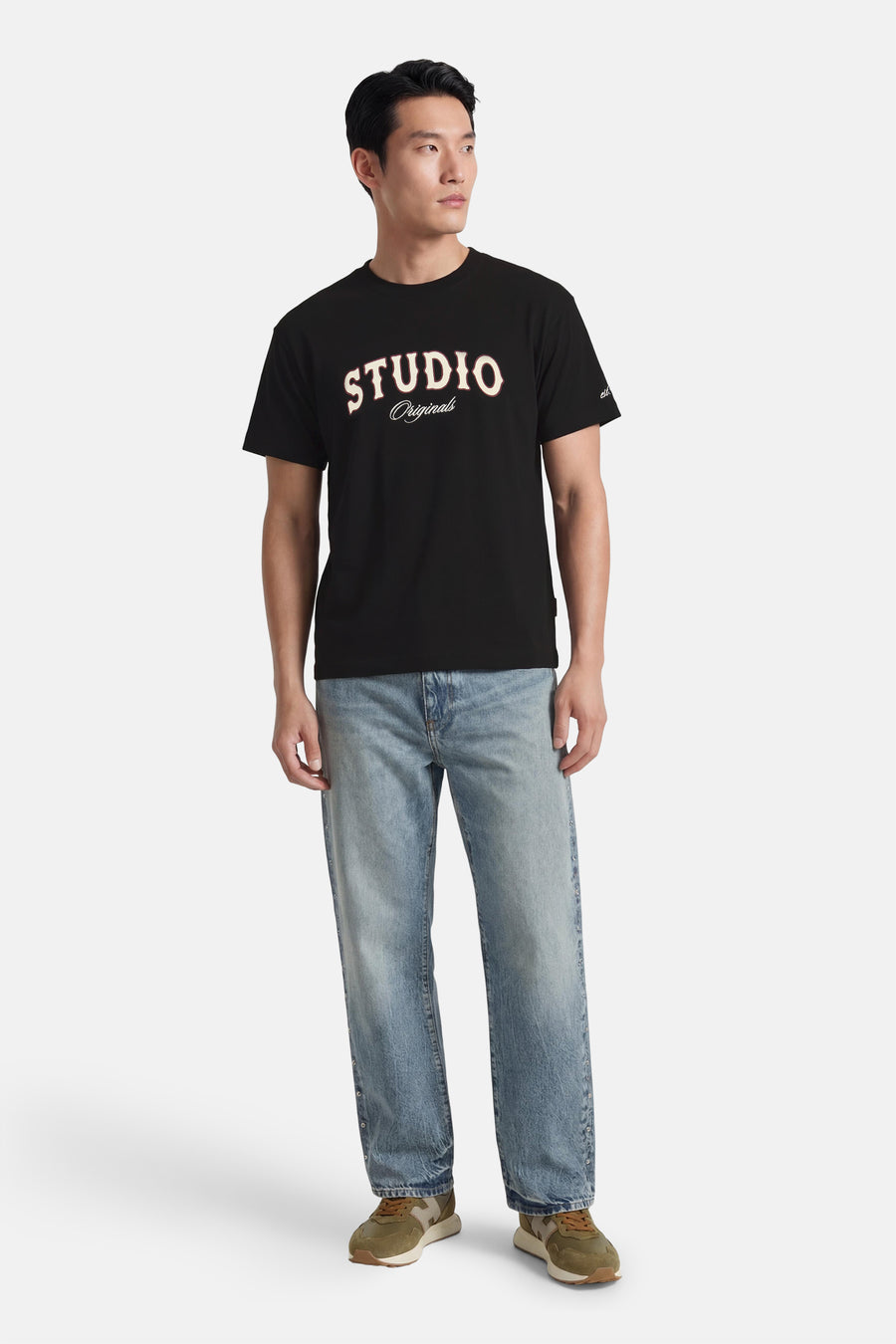 T-shirt noir à manches courtes de ORIGINALS BY JACK & JONES, avec imprimé texte blanc "STUDIO" et combiné avec un jean et des baskets vertes.