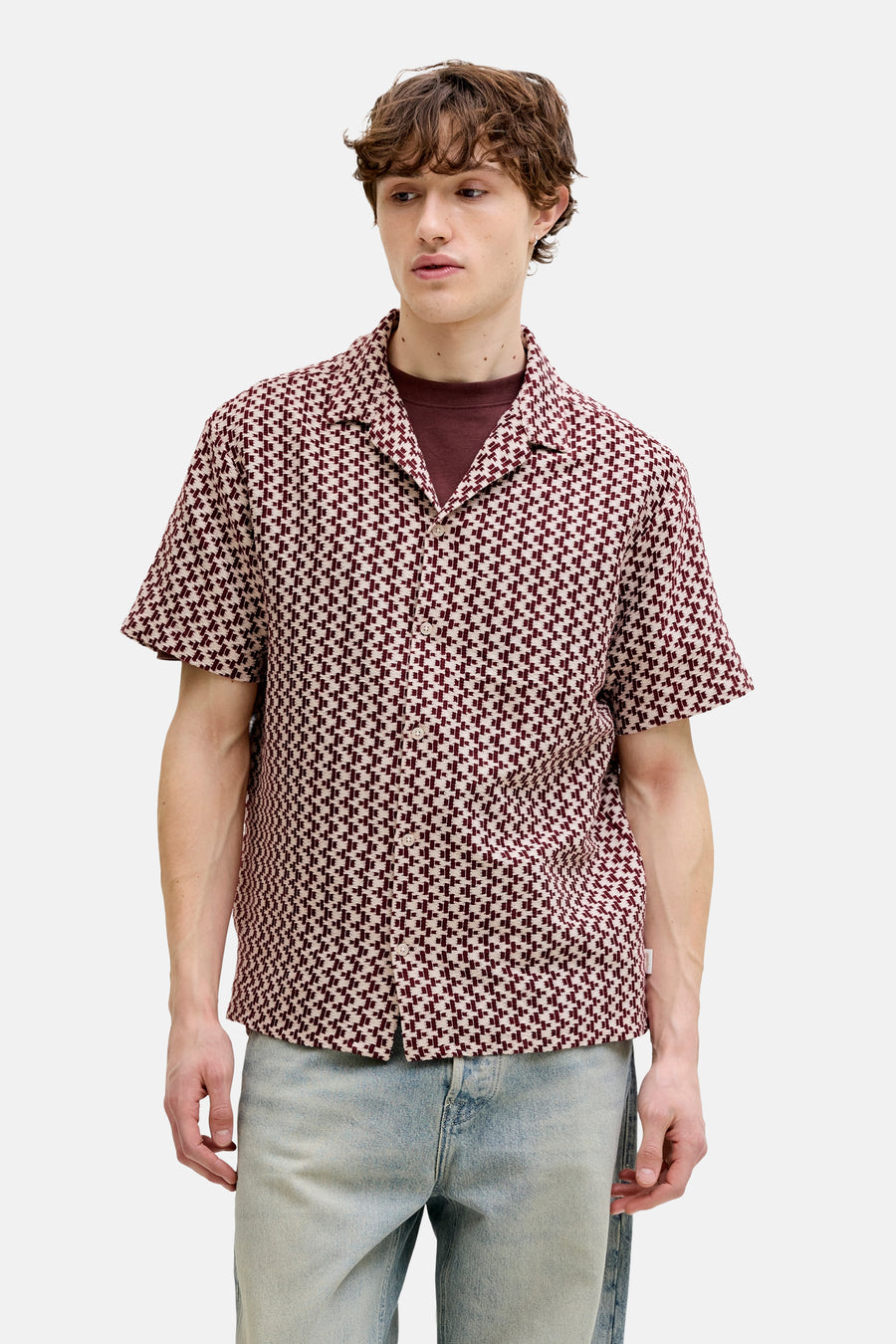 Chemise rouge à manches courtes de ORIGINALS BY JACK & JONES, avec un motif à carreaux géométriques, portée sur un t-shirt bordeaux et un jean bleu.