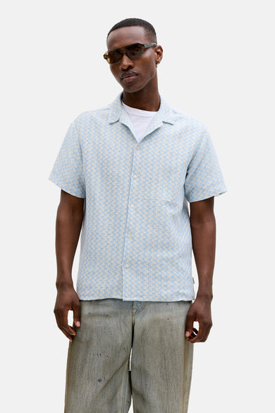 Chemise bleue à manches courtes de ORIGINALS BY JACK & JONES, avec un motif subtil, portée avec une veste beige et un t-shirt blanc.