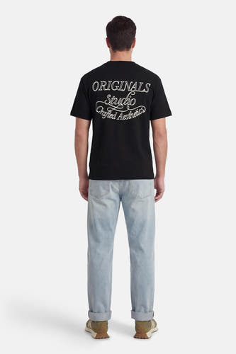 Zwart T-shirt met korte mouwen van ORIGINALS BY JACK & JONES, met witte tekstprint op de achterkant, gecombineerd met lichtblauwe jeans en groene sneakers.