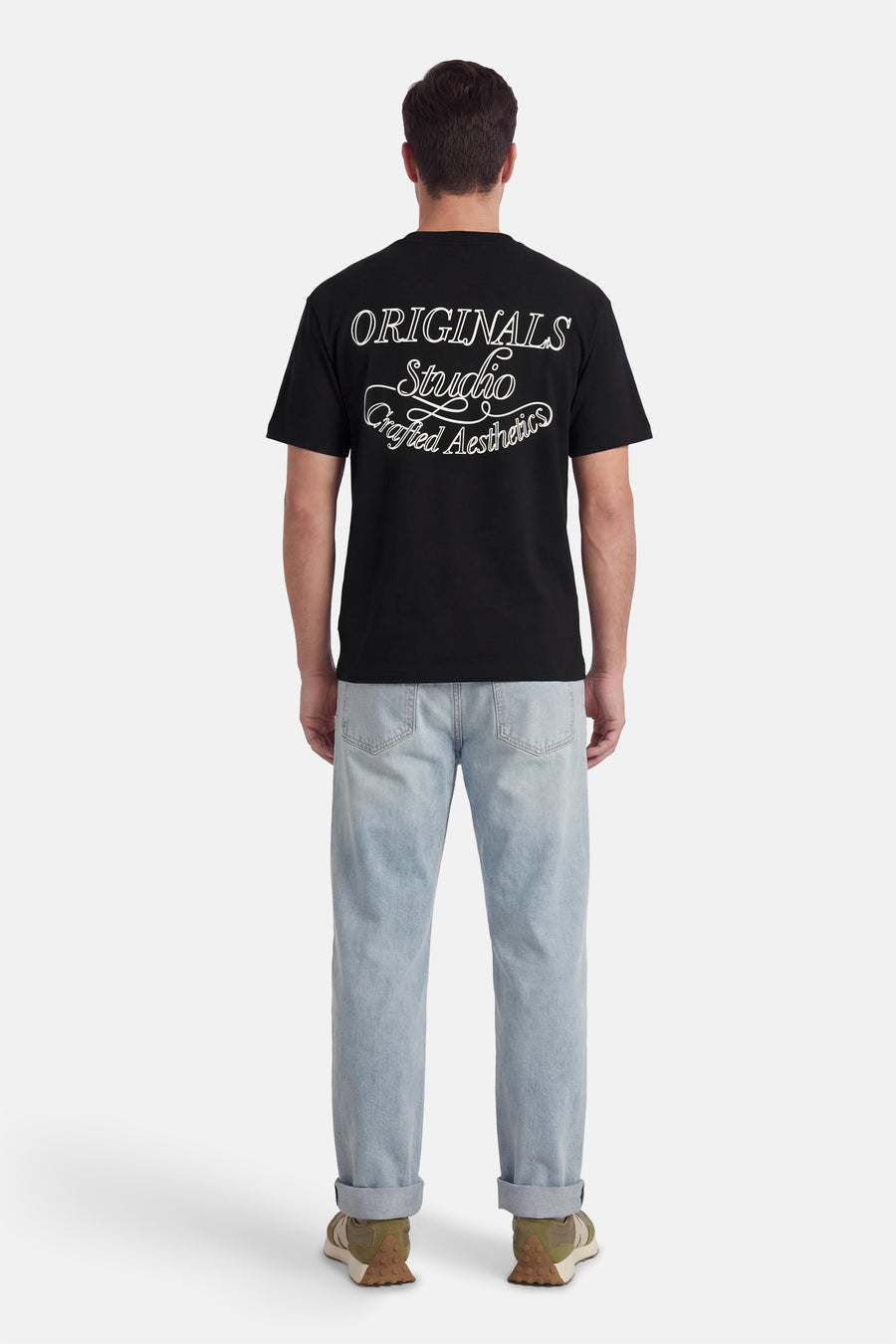 Zwart T-shirt met korte mouwen van ORIGINALS BY JACK & JONES, met witte tekstprint op de achterkant, gecombineerd met lichtblauwe jeans en groene sneakers.