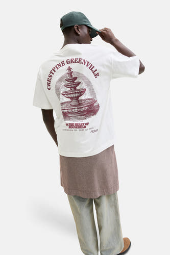 Wit T-shirt van ORIGINALS BY JACK & JONES, met grafische print op de rug en gecombineerd met een geruite rok en wijde jeans.
