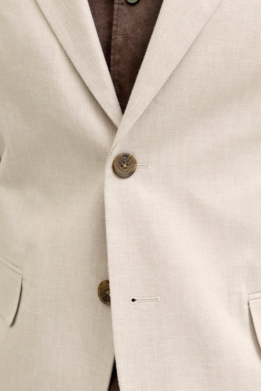Detail van een ecru blazer van PREMIUM by JACK & JONES van structuurstof, met bruine knopen en een bruin overhemd eronder.