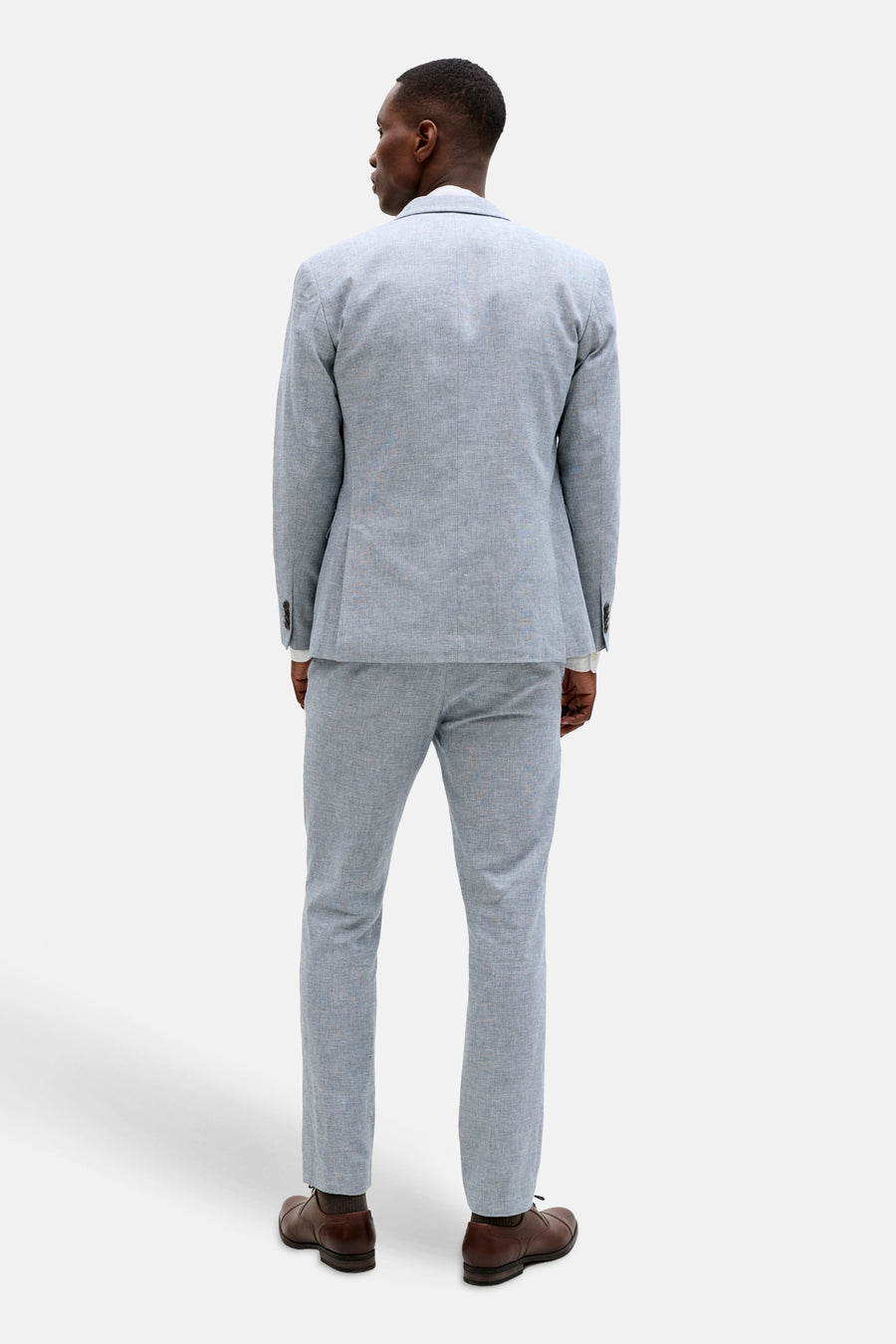 Blauwe blazer van PREMIUM by JACK & JONES met textuur, van achteren gezien, gedragen over een witte blouse met bijpassende pantalon en bruine schoenen.