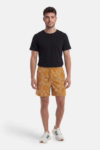 Gele zwemshort van PREMIUM by JACK & JONES met wit bloem- en ruitpatroon, gedragen door een man met zwart T-shirt en witte sneakers.