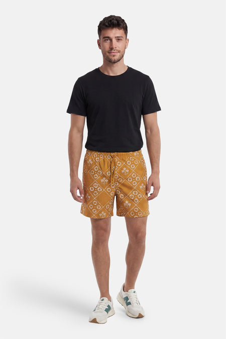 Gele zwemshort van PREMIUM by JACK & JONES met wit bloem- en ruitpatroon, gedragen door een man met zwart T-shirt en witte sneakers.