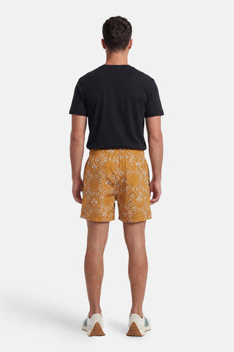 Gele zwemshort van PREMIUM by JACK & JONES met wit bloem- en ruitpatroon, van achteren gezien, gedragen met zwart T-shirt en sneakers.