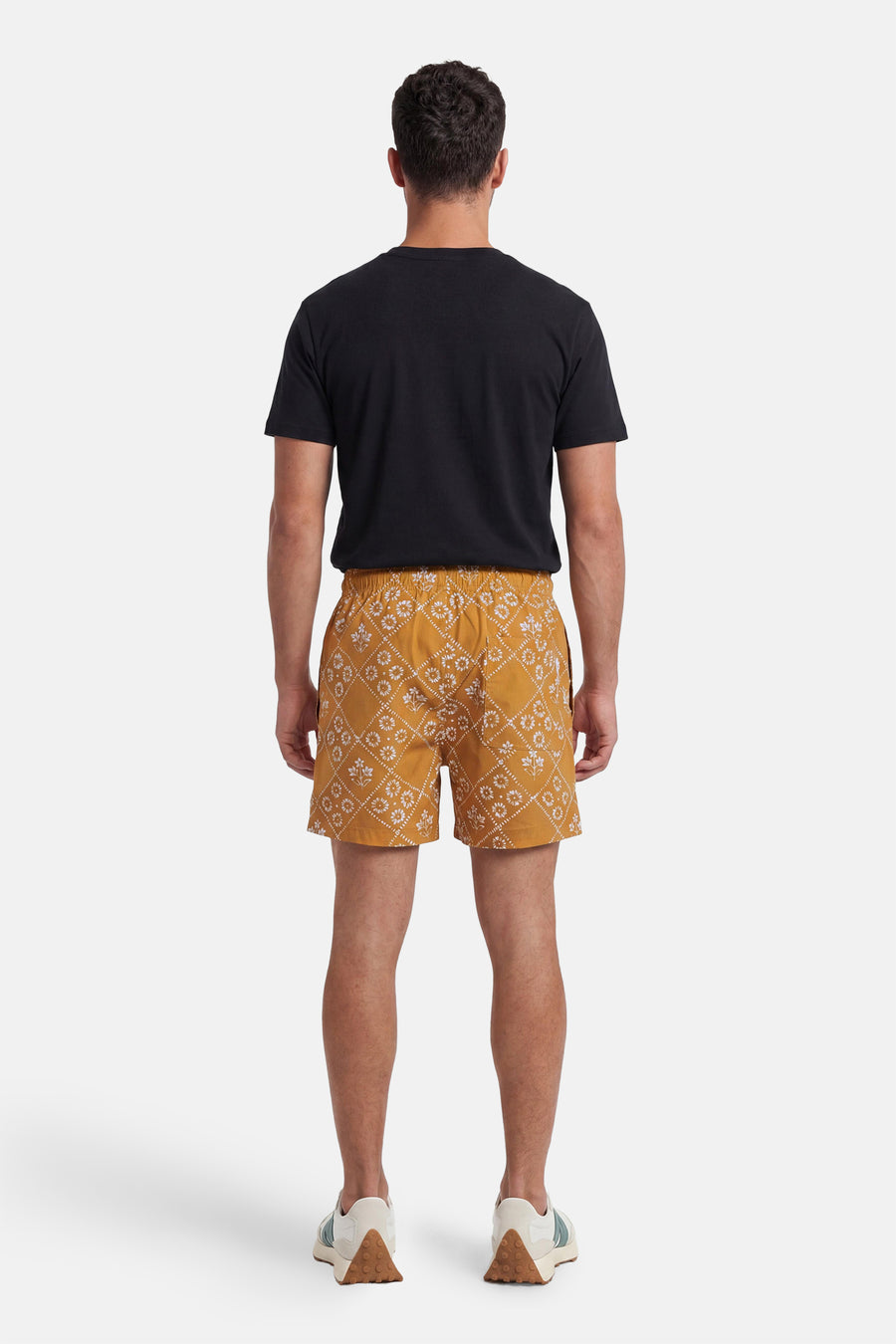 Gele zwemshort van PREMIUM by JACK & JONES met wit bloem- en ruitpatroon, van achteren gezien, gedragen met zwart T-shirt en sneakers.