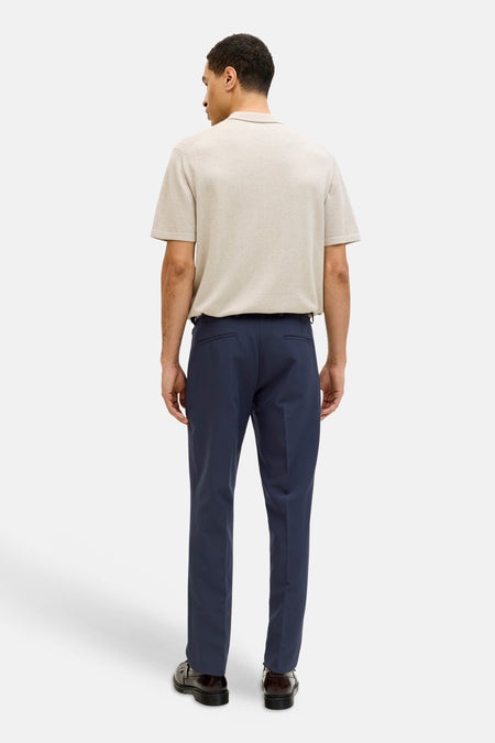 Blauwe kostuumbroek van PREMIUM by JACK & JONES, gezien van achteren, gecombineerd met een beige poloshirt en zwarte schoenen.